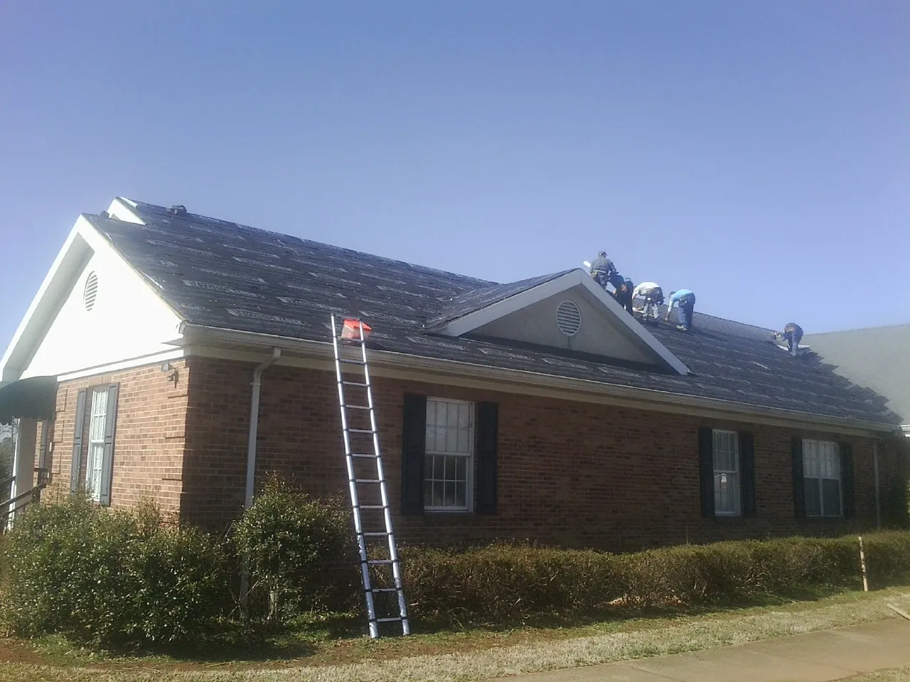 Crew tearing shingles off a brick ranch roof with a ladder set — Metal Roof Repair work by our crew in Lackawaxen