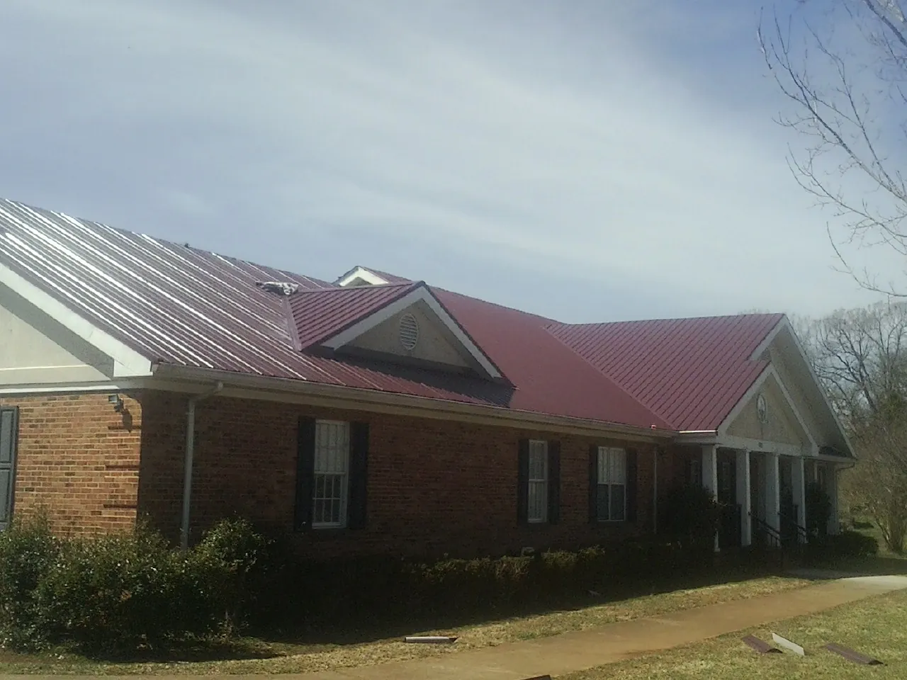 Red metal roof with gabled entries on a long brick building, from a Hail Damage Roof Repair job in Lackawaxen
