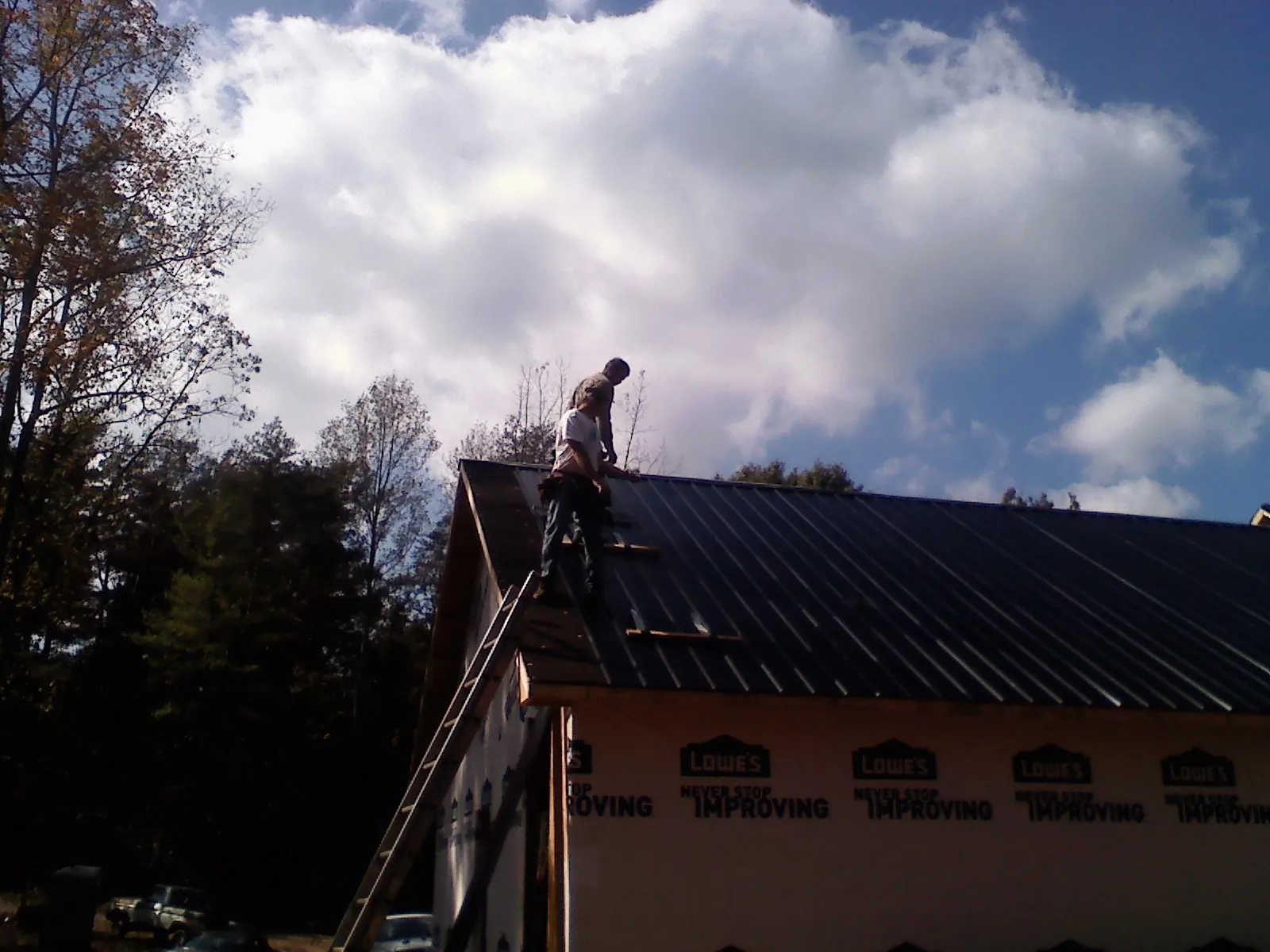 Roofer fastening dark metal panels high against a cloudy sky, from a Roof Inspection job in Lackawaxen