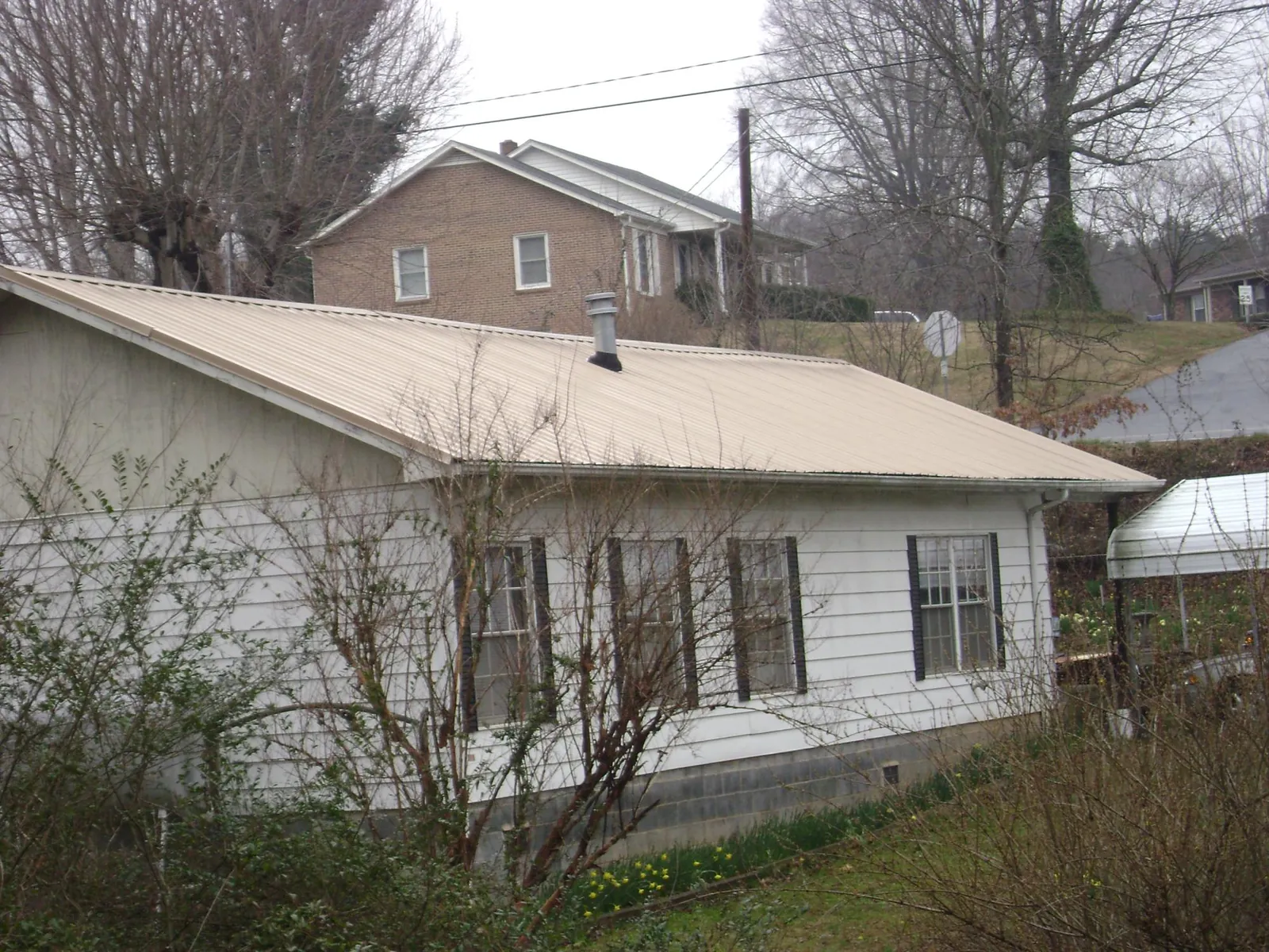 Tan metal roof on a white sided house set into a hillside — Commercial Roofing by Roofing Brothers in Lackawaxen
