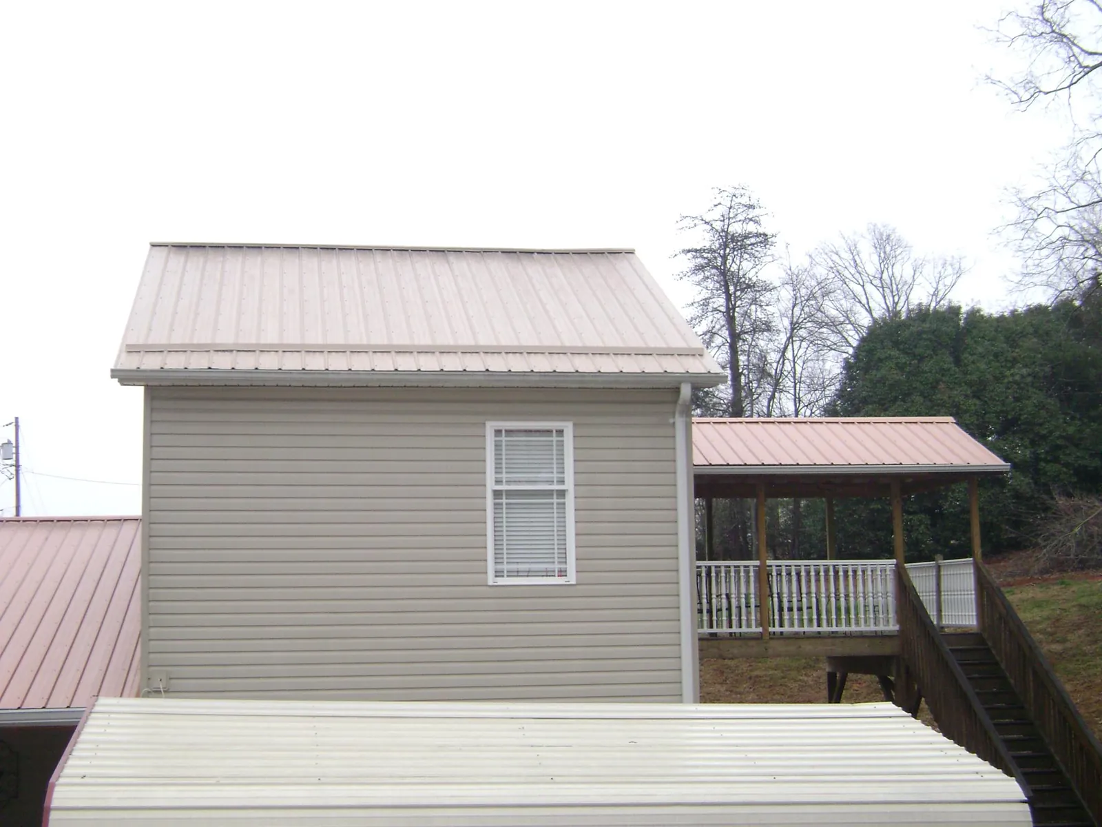 Tan metal roofs on a two story addition and attached porch, from a Roof Replacement job in Lackawaxen